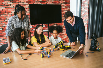 Three diverse students and two inclusive teachers collaborate on a robotics activity using electronics and a laptop, promoting STEM education, teamwork, and hands-on learning in a dynamic classroom.
