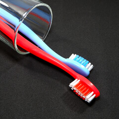 A set of colorful toothbrushes in a clear glass on black background closeup shot, conveying a sense of oral hygiene and daily routine with a touch of vibrancy.