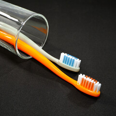 A set of toothbrushes in a clear glass on black background closeup shot, conveying a sense of oral hygiene and daily routine with a touch of vibrancy.