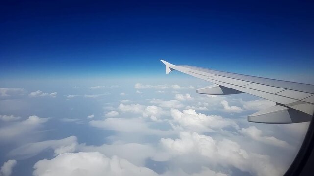 Close up of airplane wing tip soaring through clear deep blue sky and white clouds. High altitude flight view from passenger window. Aerial transportation and global travel background.