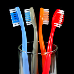 A set of colorful toothbrushes in a clear glass on black background closeup shot, conveying a sense of oral hygiene and daily routine with a touch of vibrancy.