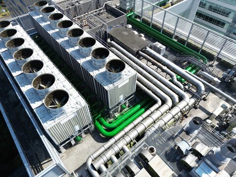 Aerial view of complex industrial piping and cooling towers on a building rooftop.