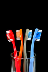 A set of colorful toothbrushes in a clear glass on black background closeup shot, conveying a sense of oral hygiene and daily routine with a touch of vibrancy.