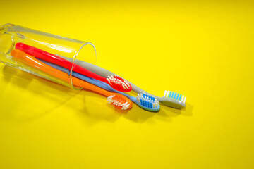 Colorful toothbrushes in a clear glass red, orange, blue, and grey on a sleek yellow background, evoking a sense of cleanliness and oral health, Daily routine concept photography