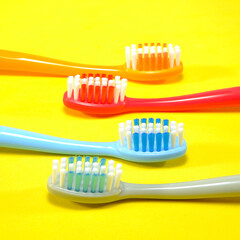 Vibrant toothbrushes in red, orange, blue, and grey arranged on a sleek yellow background, evoking a sense of cleanliness and oral health, Daily routine concept photography