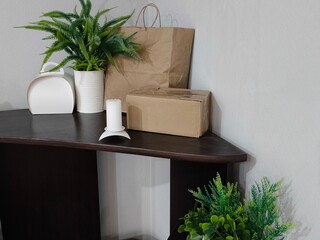 Empty blank product packaging with green plant and burning candle on wooden shelf. Delivery, unboxing, home decor concept.