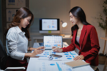 Fototapeta premium Two professional businesswomen are collaborating, analyzing financial data and reports using a tablet and papers while working together in a modern office