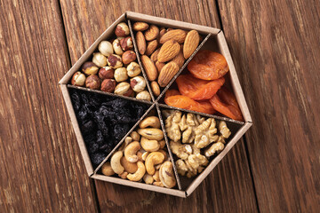 Assorted nuts and dried fruits in a cardboard box on a wooden table, top view, authentic photograph, not AI-generated