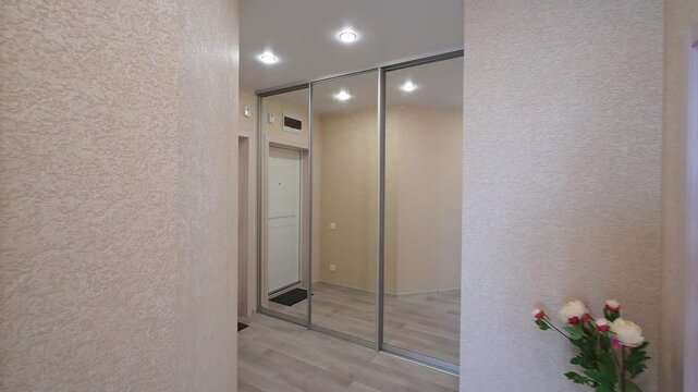 Narrow hallway with beige textured walls, white door, mirrored sliding wardrobe, small ventilation grilles, neutral tones, clean lines, minimal decor, practical layout.