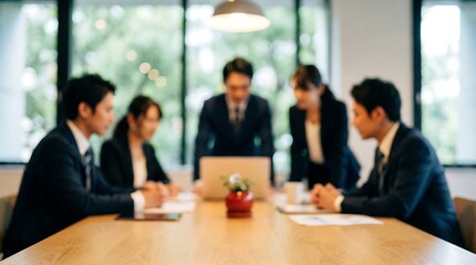 A focused group of Japanese business professionals attentively participates in a productive corporate meeting around a wooden table in a well-lit office.
