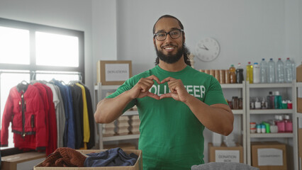 Man forms heart with hands over a donation box in a building volunteer room; community support compassion.