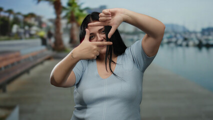 Woman gestures creatively on a seaside promenade, embracing her carefree, curvy style with a playful expression by the beach, surrounded by a serene outdoor backdrop.