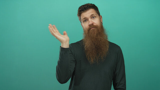 Man with long brown beard raises bare hand with open palm against a teal studio background; curiosity.