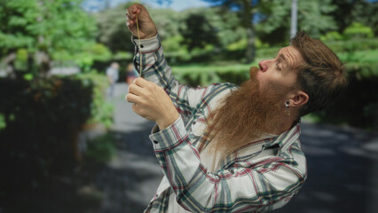 Naklejka premium Man with long red beard extends yellow measuring tape along leafy street walkway under sunlight; precision.