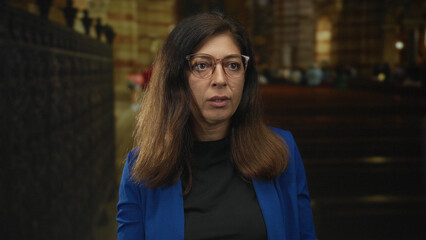 Woman adjusts eyeglasses inside church building and looks forward with steady gaze; quiet contemplation.