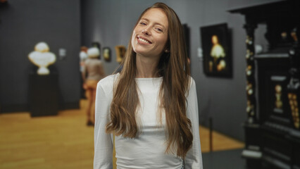 Woman with long hair and visible face standing by paintings inside art gallery building; thoughtful...