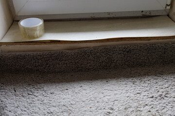 A worn window sill shows a piece of tape on the edge, with carpet below displaying signs of use