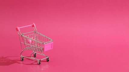 Positioning empty metal cart against vivid pink backdrop, highlighting shopping theme.