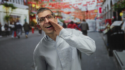 Fototapeta premium Man wearing glasses and striped shirt smiling and speaking on busy outdoor street with red decorations in background, capturing lively urban scene in daylight.