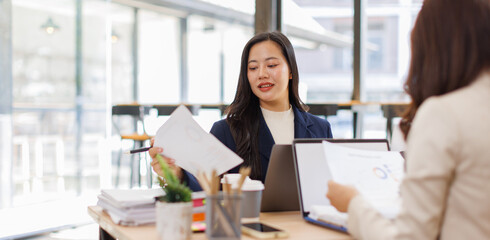 Asian business team colleagues analyzing financial charts and data on computer screen in a bright modern office.
