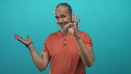Man points finger to open palm and makes ok sign in studio with turquoise backdrop; presentation approval playful.