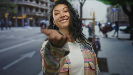 Fototapeta premium Young hispanic woman smiling with hand extended palm up beckoning on a busy city street in daylight; friendly invitation.