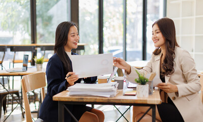 Asian business team colleagues analyzing financial charts and data on computer screen in a bright modern office.
