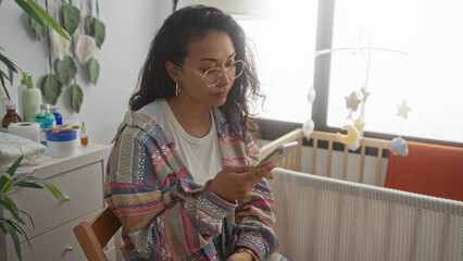 Woman holding smartphone beside a baby crib in a nursery inside a building; contemplation motherhood.