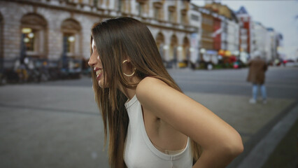Woman leaning in white tank top with arm bent and hands on hips on busy city street lined with historic restaurant arches; confidence.