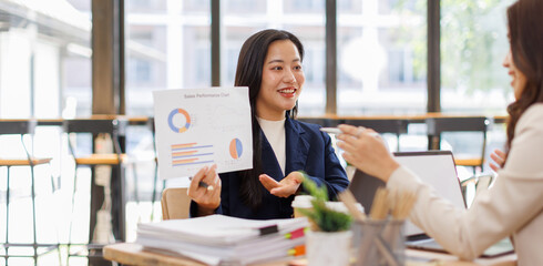 Asian business team colleagues analyzing financial charts and data on computer screen in a bright modern office.
