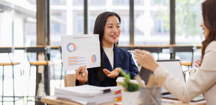 Asian business team colleagues analyzing financial charts and data on computer screen in a bright modern office.
 - Powered by Adobe