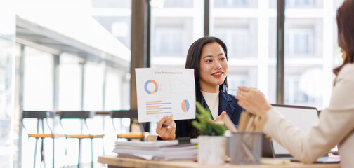 Asian business team colleagues analyzing financial charts and data on computer screen in a bright modern office.