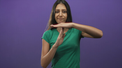 Young hispanic woman in green shirt with hands making time out gesture in purple studio; disapproval restraint.
