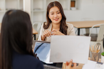 Asian business team colleagues analyzing financial charts and data on computer screen in a bright modern office.
