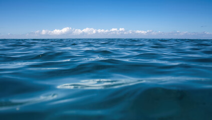 Fototapeta premium Calm blue ocean surface with distant clouds and clear sky, serene natural seascape
