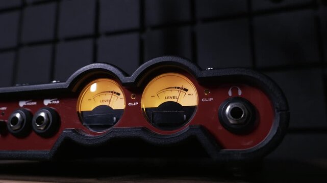 Close up of analog VU meters on a professional audio interface, with needles moving to the sound level. Concept of music production, sound engineering, recording, and professional audio equipment.