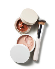 Two cosmetic cream pots with rich textures and a professional foundation blending brush