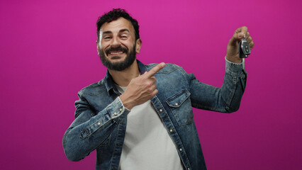 Man with beard smiles holding car keys against vibrant pink backdrop showcasing casual denim style