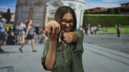 Obraz premium Young woman holds model brain and points finger at building near pisa tower plaza; curiosity education learning.