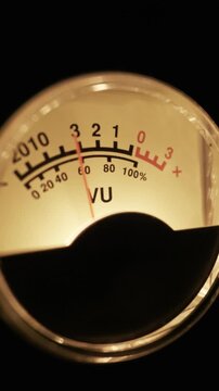 A close-up of a warm, glowing analog VU meter shows the needle measuring sound volume. Concept of music production, audio mixing, broadcasting, and vintage electronics.