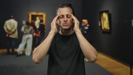 Man young hispanic with raised hand looking at camera among paintings in gallery building;...