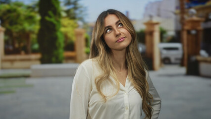 Fototapeta premium Young blonde woman face with long hair over shoulders looks upward in sunlit stone courtyard; curiosity reflection.