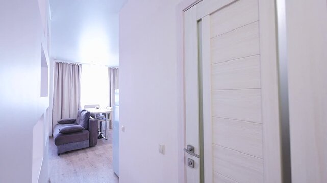 modern interior with a white door, a cozy grey sofa near a small table, light curtains, and a minimalist design; viewed from a hallway