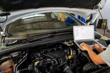 Auto mechanic performing car diagnostics using laptop under open hood