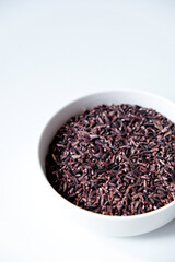 A bowl of black sticky rice grains isolated on white background