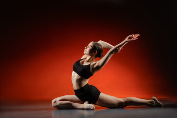 Female dancer stretching in floor split pose on red studio background copyspace