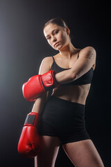 Female boxer posing with red gloves in dark studio, vertical composition