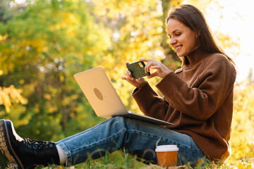 Female user scanning QR code from laptop with smartphone in park