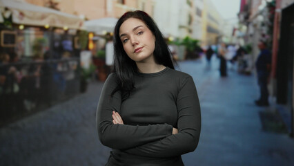 Fototapeta premium Woman standing with crossed arms on bustling street showcasing urban life with casual confidence and brunette hair.
