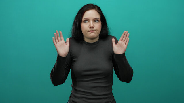 Woman brunette shrugging uncertainly against vibrant blue background emphasizing confusion and questioning with gestures.